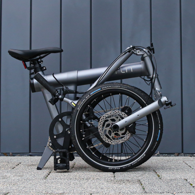 FLIT M2 folding ebike, folded in front ogf a grey wall in Cambridge
