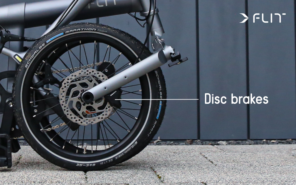 FLIT M2 folding ebike disc brakes image against a grey panelled wall